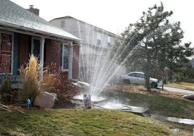 A sprinkler watering a lawn outside a house on a sunny day.